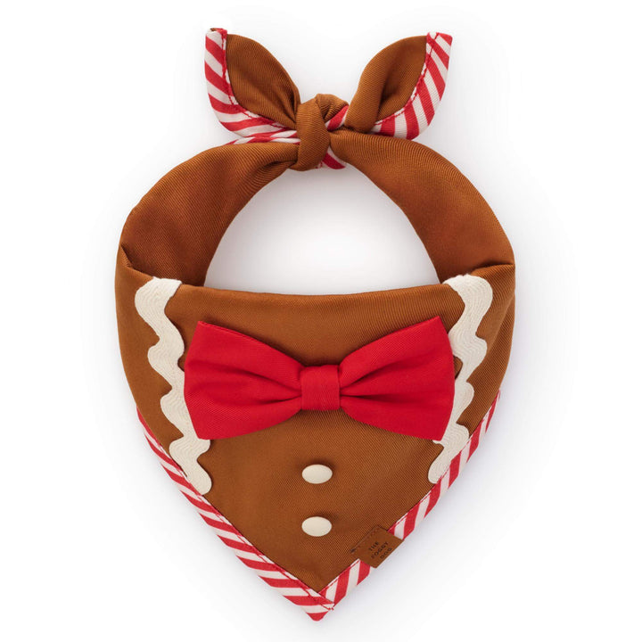 Brown gingerbread-style dog bandana with red bow, two white buttons, white icing trim, and red-and-white striped edging.