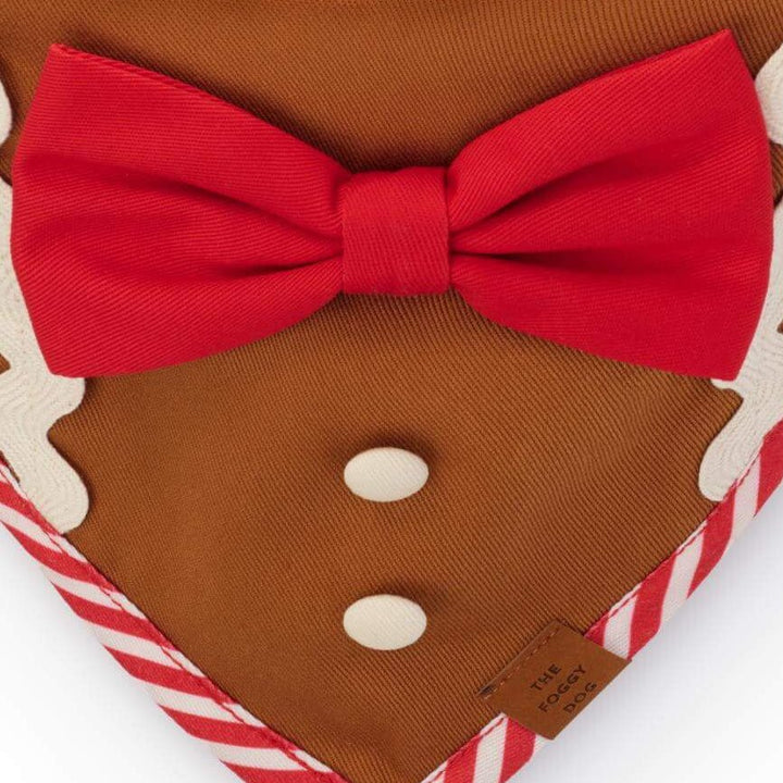 Close-up of the red bow, two white buttons, icing-like trim, and striped edge on the brown gingerbread dog bandana.
