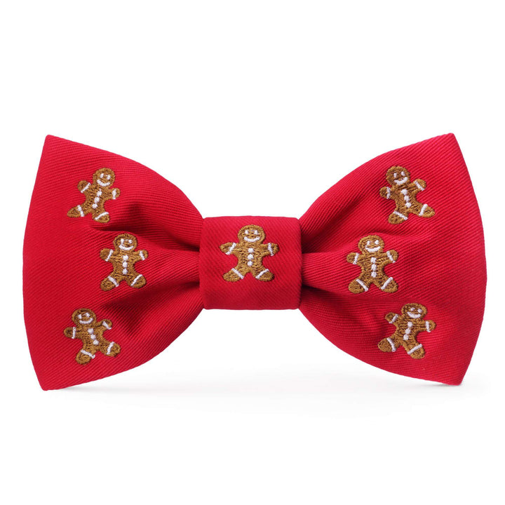 Bright red dog bow tie embroidered with smiling brown gingerbread figures and white icing details on white.