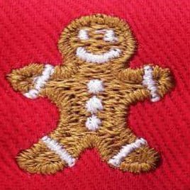 Close-up of a brown gingerbread figure with white icing stitched onto red bow-tie fabric.