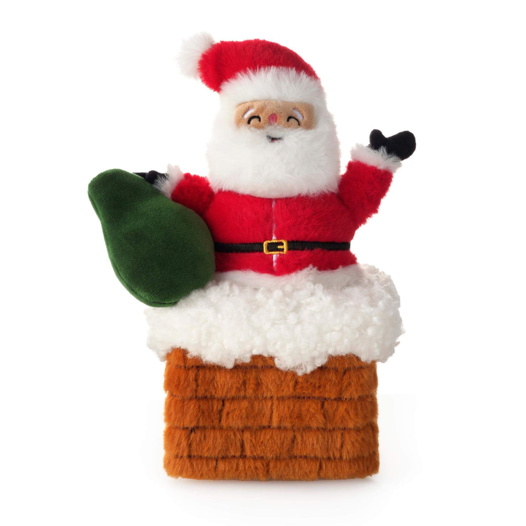Plush Santa dog toy with green sack seated in a brown brick chimney topped with fluffy white snow.