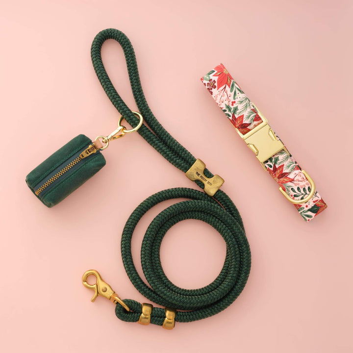 Poinsettia collar, green rope leash, and green bag holder arranged on a blush pink backdrop