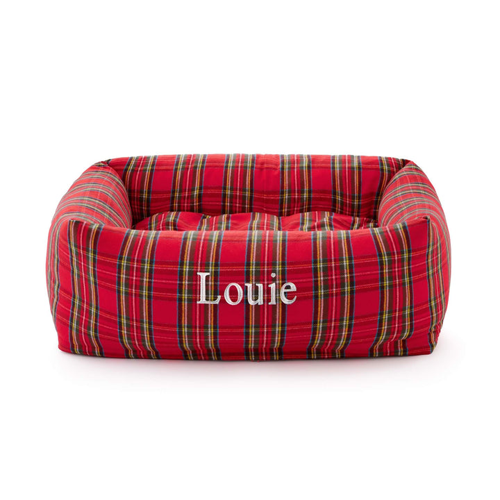 Red tartan bolster dog bed embroidered with the name Louie in white on the front, on white