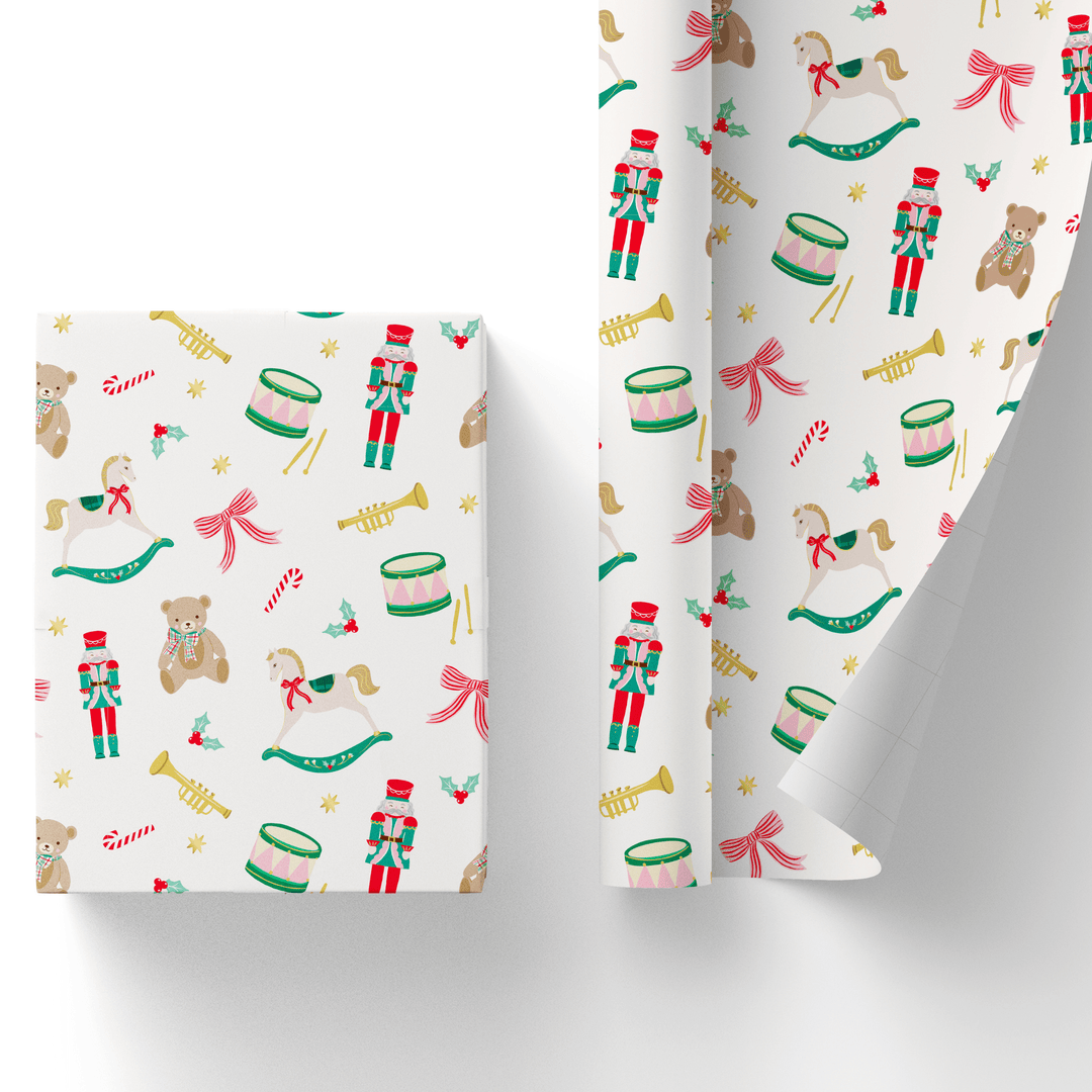 Cream Christmas gift wrap with a holiday toy print of nutcrackers, teddy bears, rocking horses, drums, and candy canes