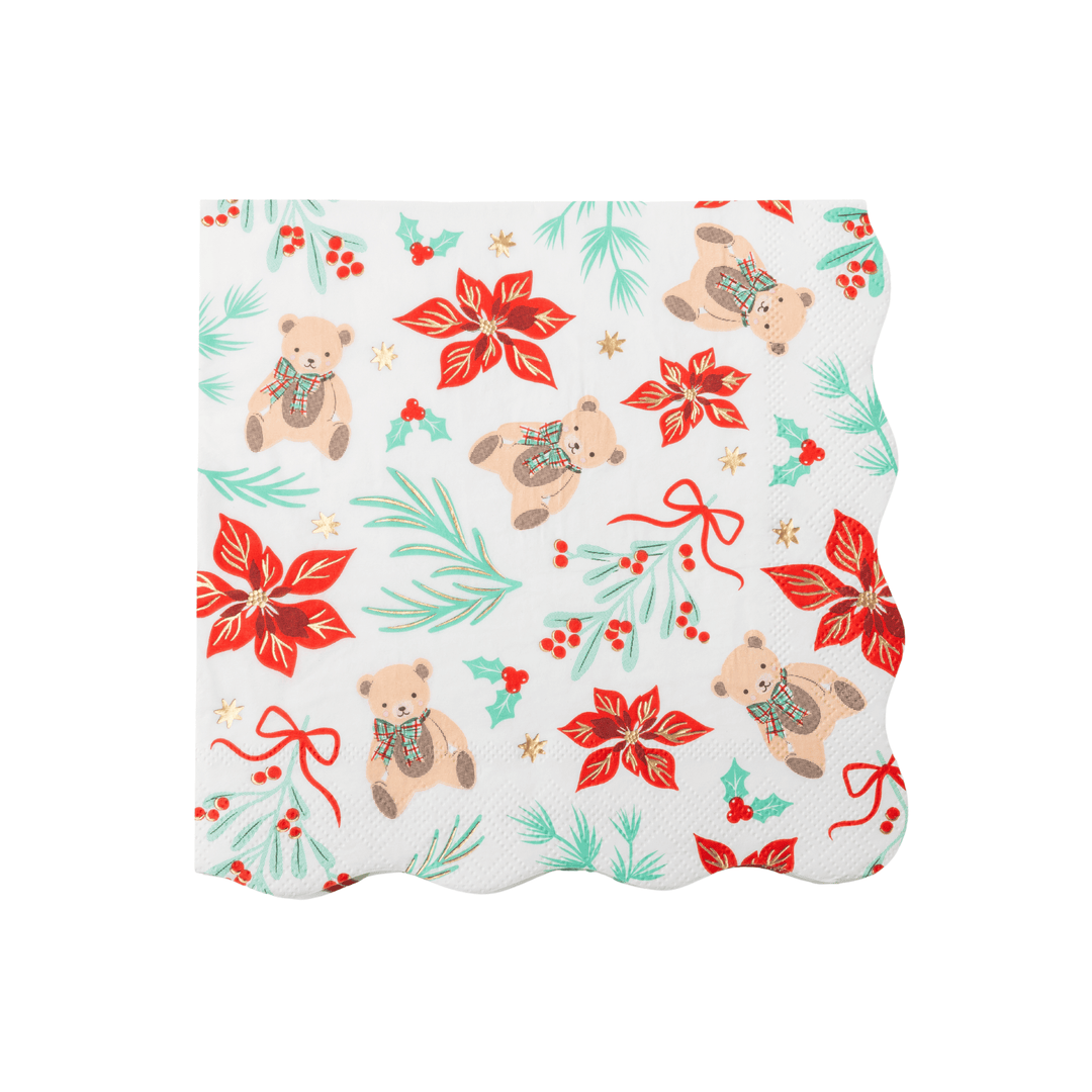 A square white paper napkin with a scalloped edge, featuring a festive Christmas pattern of teddy bears, red poinsettias, green pine branches, holly leaves, and red berries on a white background.
