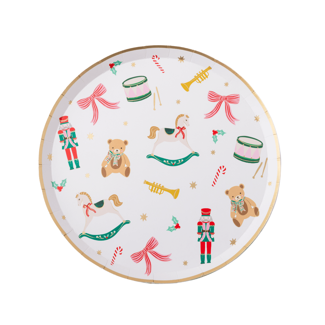 A round white paper plate decorated with a festive Christmas theme, featuring illustrations of teddy bears, nutcrackers, rocking horses, candy canes, bows, and gold stars, finished with a gold rim.