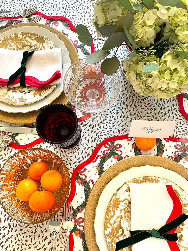 Round placemat with a scalloped edge and a red holiday wreath design