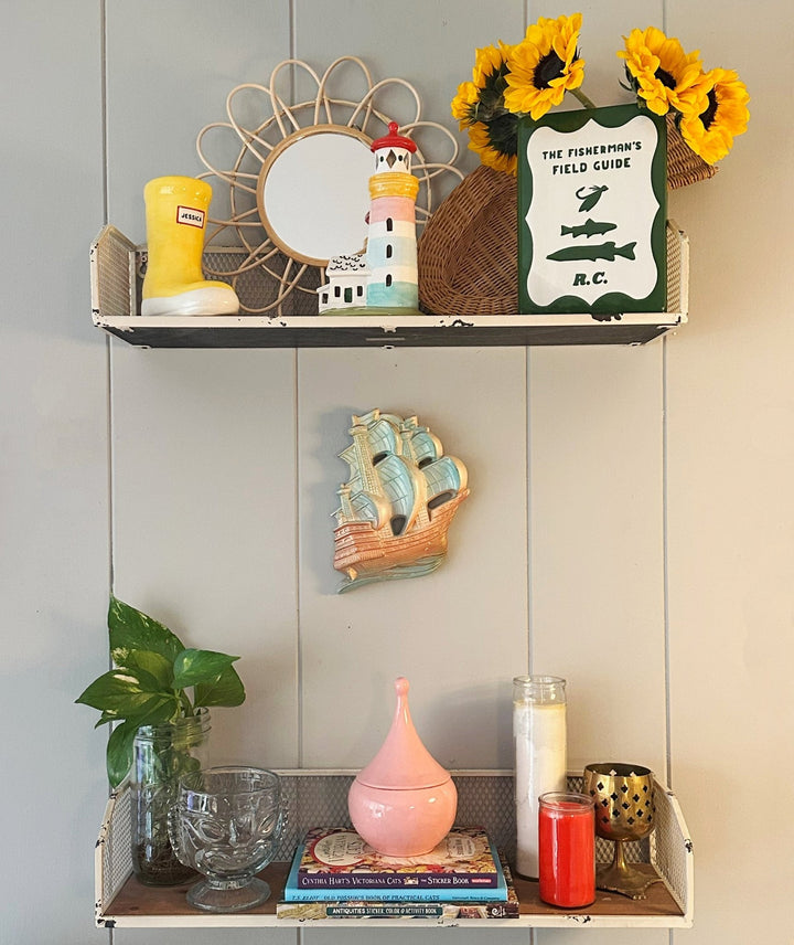 Decorative shelf with various items including a mirror, candles, and books against a gray wall.
