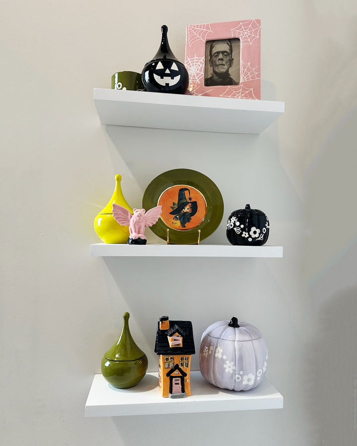 Decorative Halloween-themed shelves with various small objects on a plain wall.