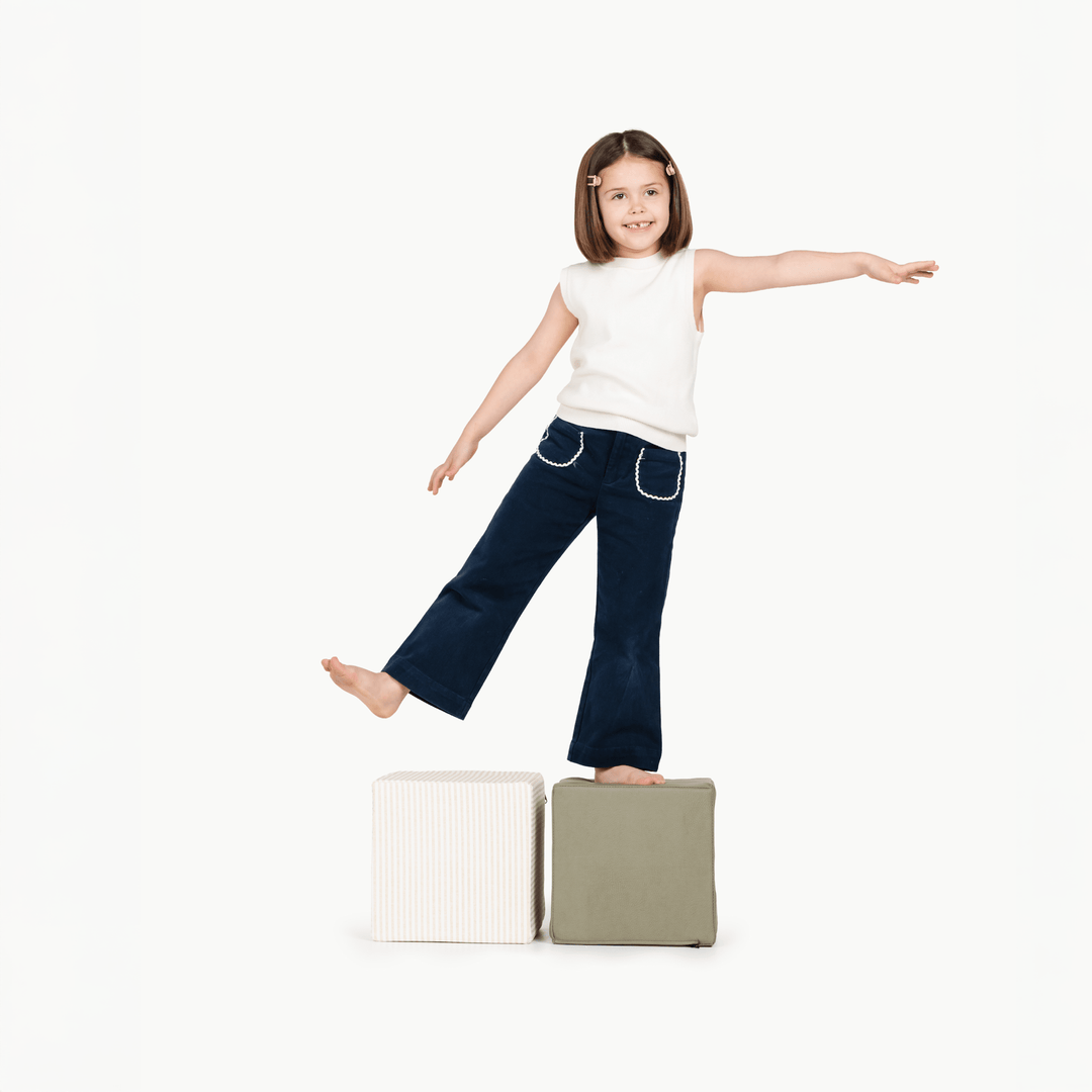Child balancing on olive and pinstripe foam play cubes for gross-motor play.
