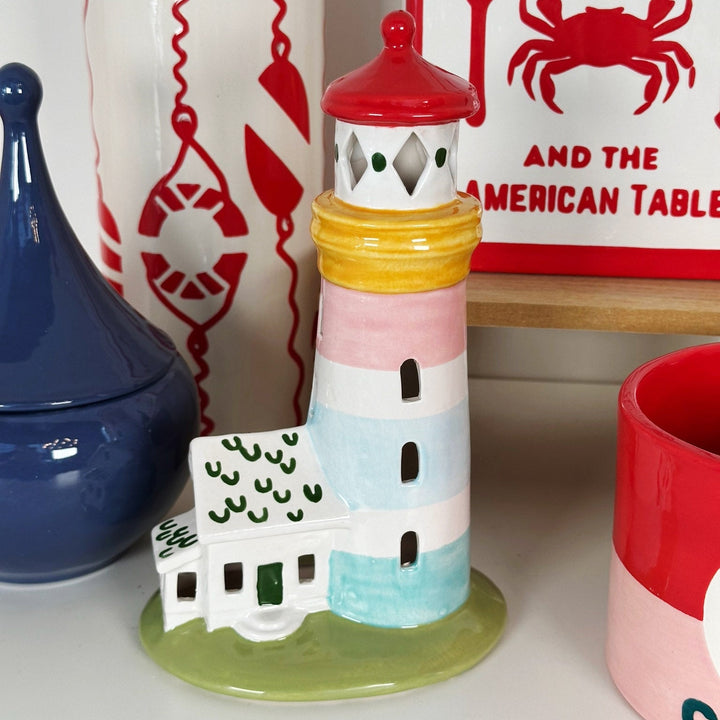 Colorful ceramic lighthouse on a surface with a blue vase and red mug in the background.