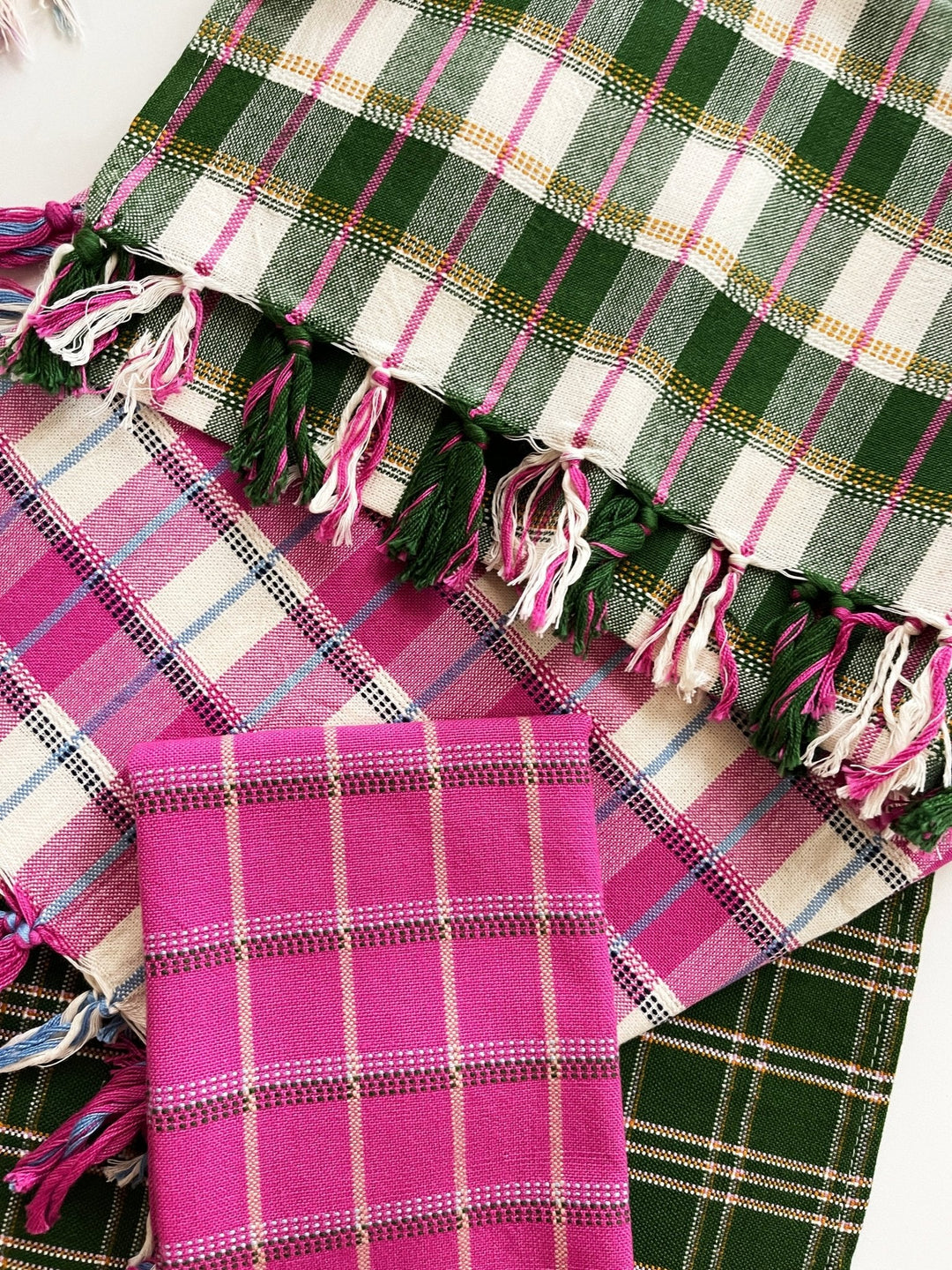 Forest green plaid towel draped over pink and dark green woven textiles