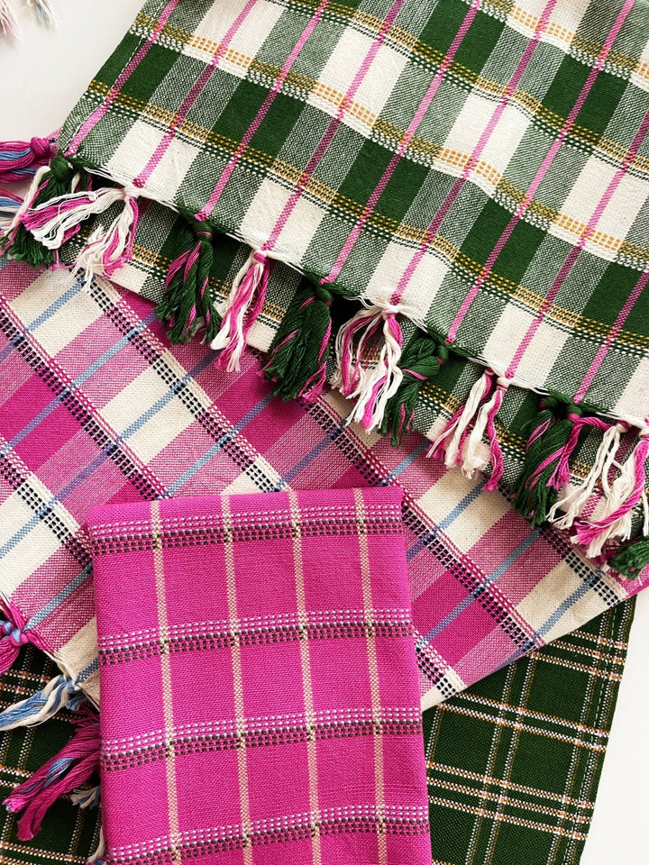 Forest green plaid towel draped over pink and dark green woven textiles