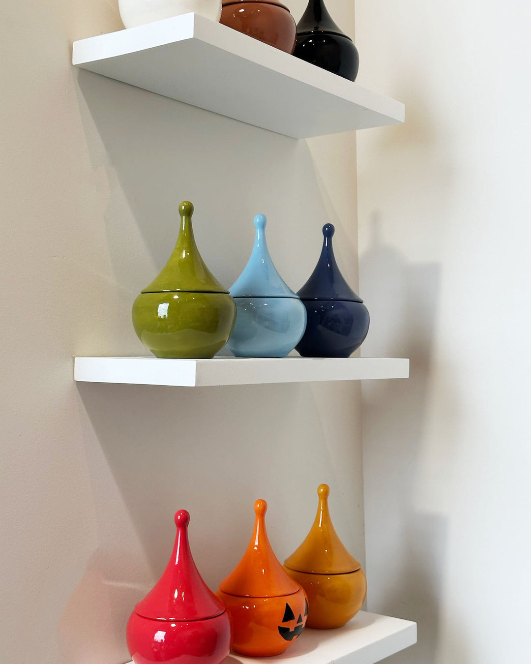 Colorful ceramic jars on a white shelf against a beige wall