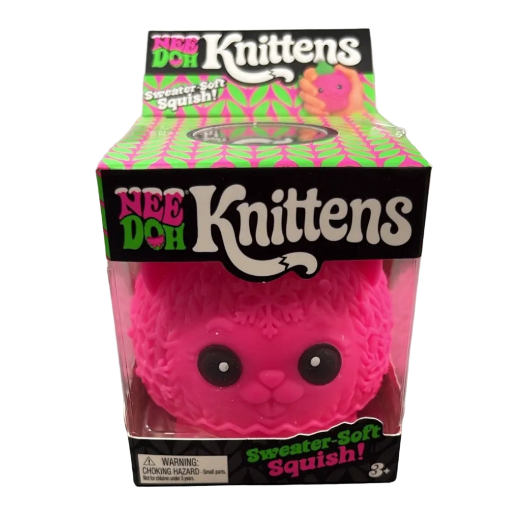 A pink fuzzy squishy toy in its original retail packaging, featuring the 'Nee Doh Knittens' brand. The toy is visible through a clear plastic window on a gray mottled countertop.