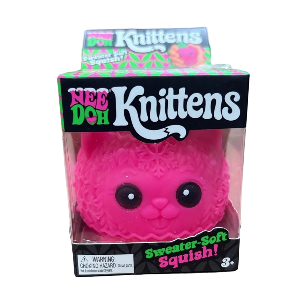 A pink Knittens 'Sweater-Soft Squishy' toy in its original retail packaging, displayed on top of cardboard boxes.