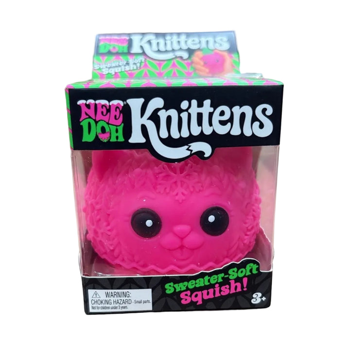 A pink Knittens 'Sweater-Soft Squishy' toy in its original retail packaging, displayed on top of cardboard boxes.