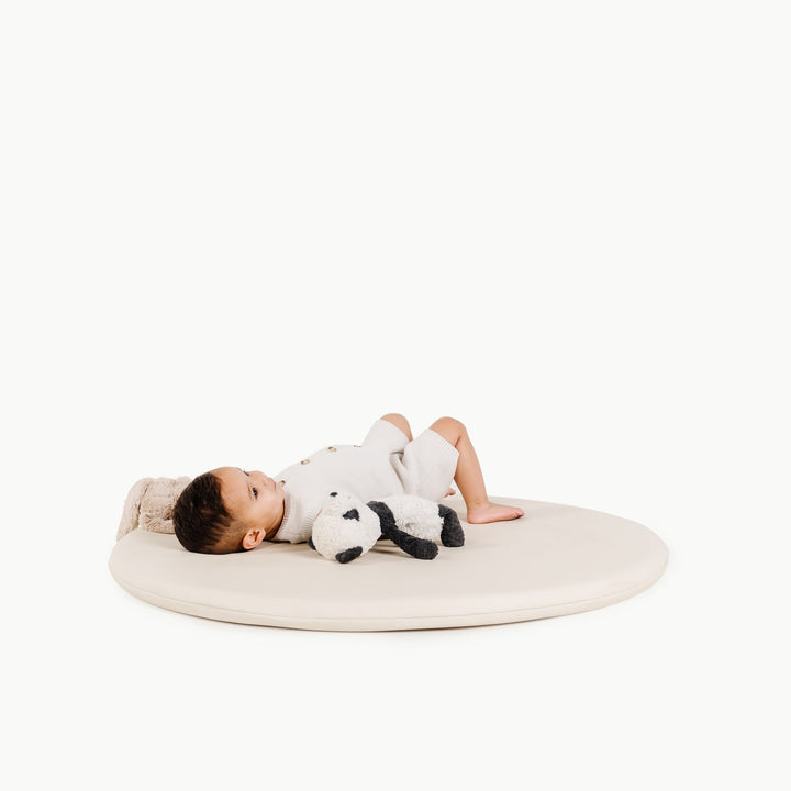 Cream round padded baby play mat with a baby resting on it during tummy time.