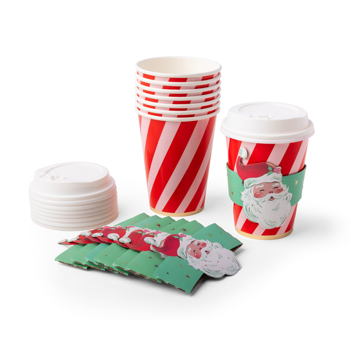 Christmas-themed paper coffee cups and lids with Santa Claus designs, including a stack of red-and-white striped cups, a single cup with a green Santa sleeve, loose white lids, and green napkins on a white background.