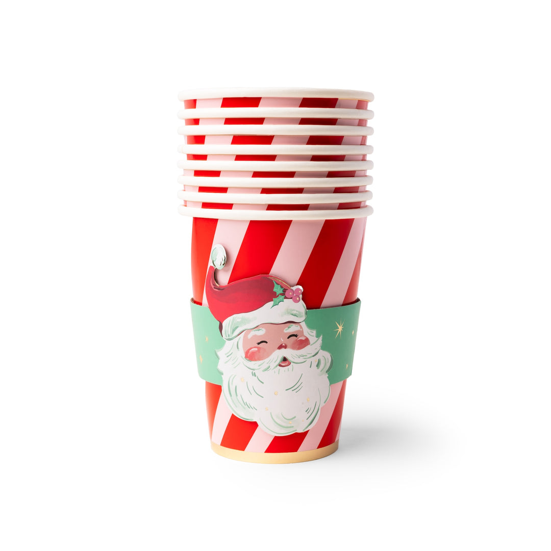 A stack of paper cups with red and white diagonal stripes, decorated with a green Santa hat and beard sleeve, on a white background.