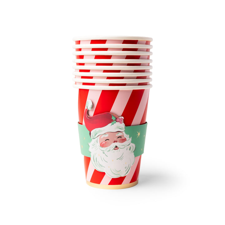 A stack of paper cups with red and white diagonal stripes, decorated with a green Santa hat and beard sleeve, on a white background.