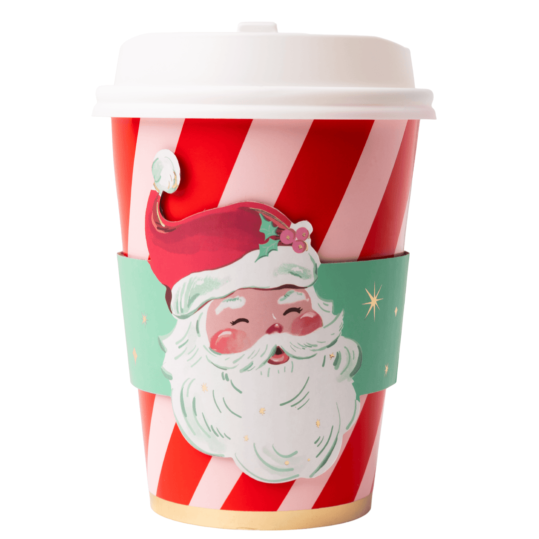 A festive disposable coffee cup with red and white diagonal stripes, a white lid, and a mint green silicone sleeve featuring a large illustrated Santa face.