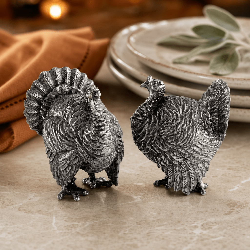 Pewter turkey salt and pepper shakers on a marble table beside stacked plates and a rust napkin