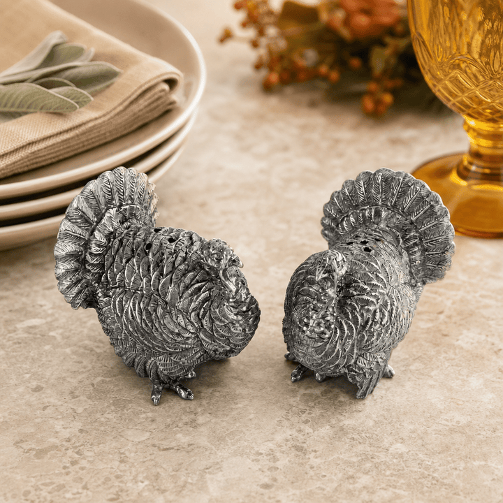 Back view of the pewter turkey shakers showing layered tail feathers, with sage and an amber glass