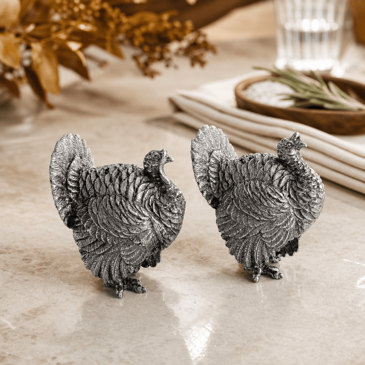 Pewter turkey salt and pepper shakers facing each other on a fall table set with linen napkins