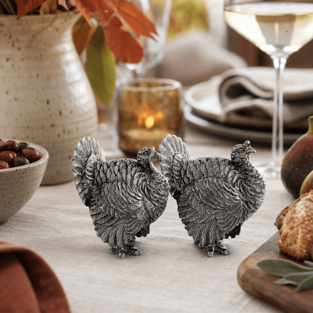 Pewter turkey shakers side by side on a fall table with a stoneware vase and white wine