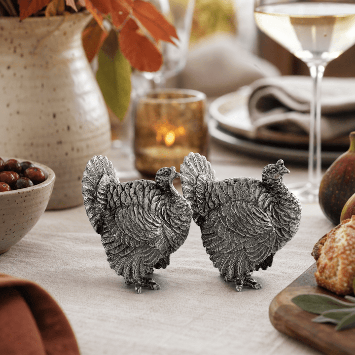 Pewter turkey shakers side by side on a fall table with a stoneware vase and white wine