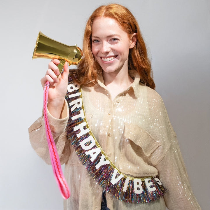 Smiling woman in a Birthday Vibes sash holding up the gold party megaphone