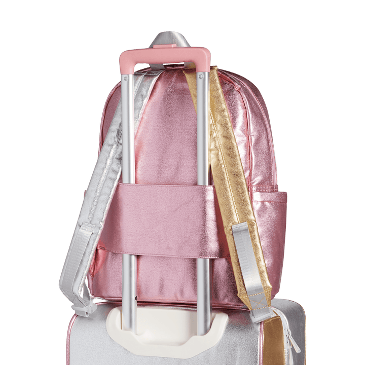 Back of the Pink/Silver Kane backpack slid over a rolling suitcase handle by its luggage sleeve