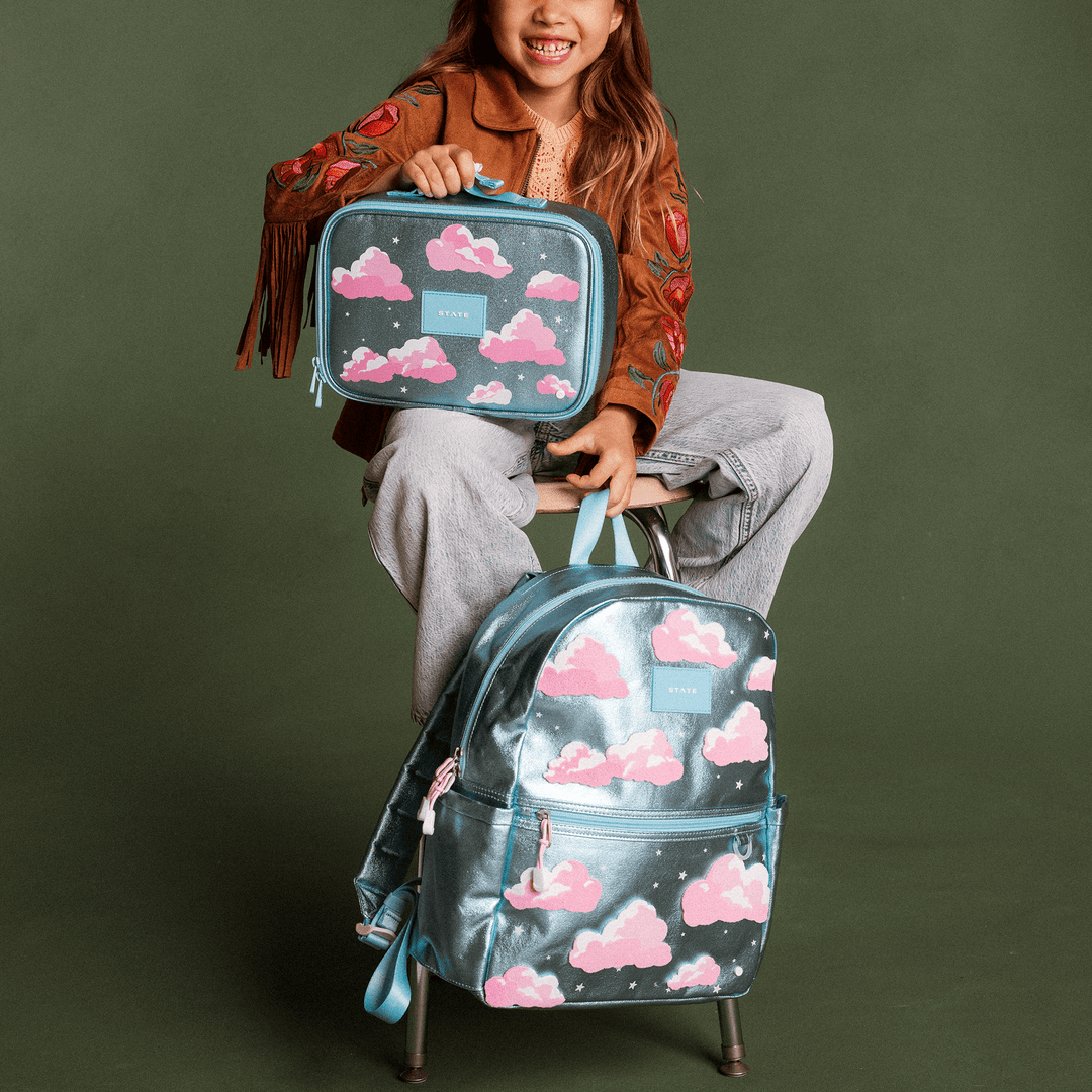 Girl seated with the Clouds backpack and matching Clouds lunch box
