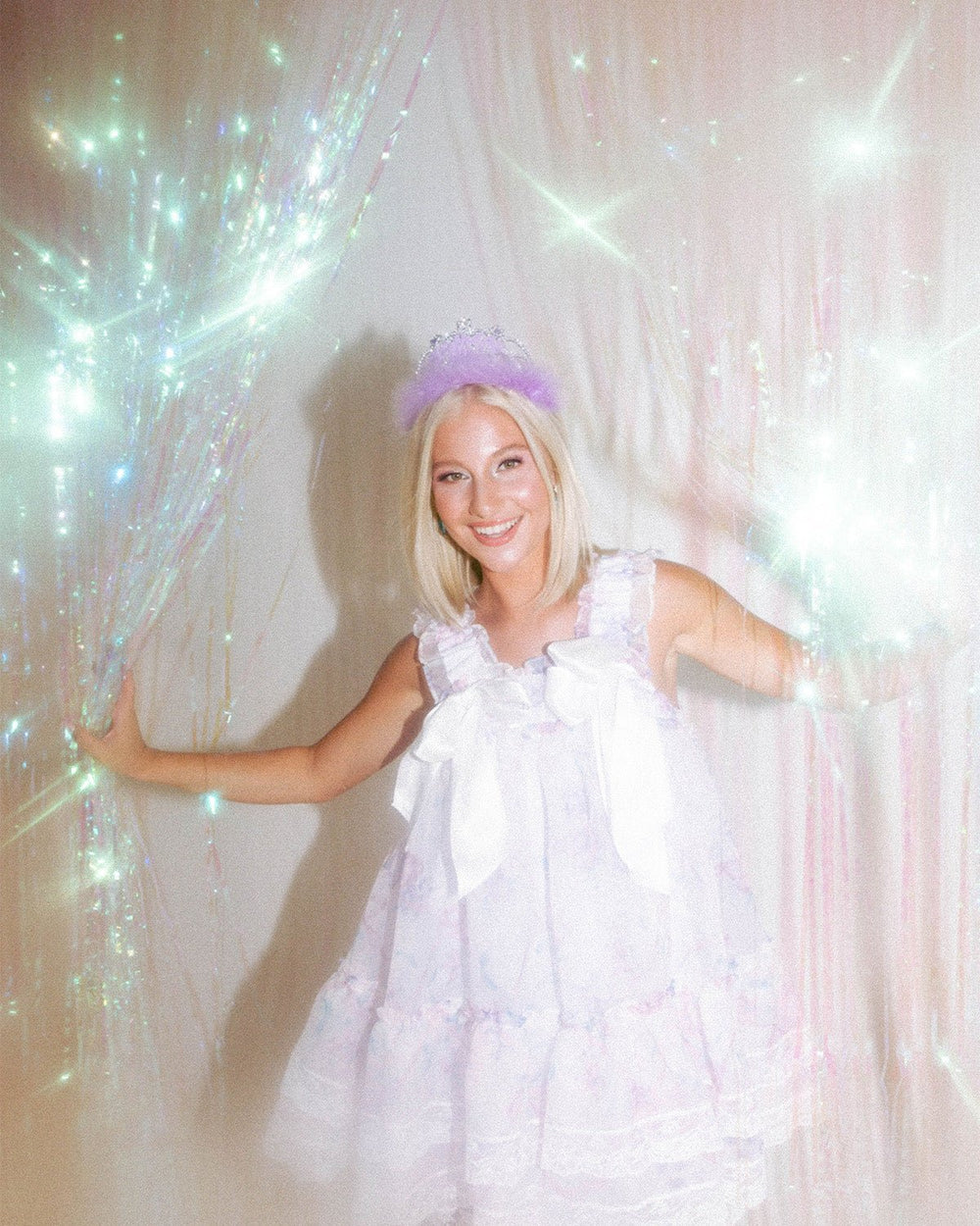Girl in a white dress standing in front of a sparkling iridescent fringe curtain backdrop