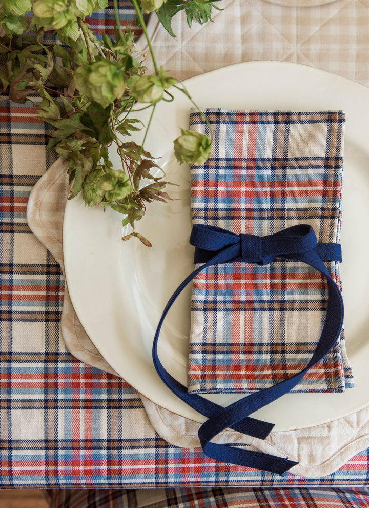 Laurel plaid cloth napkin in cream, red, and blue folded on a plate with a navy ribbon bow