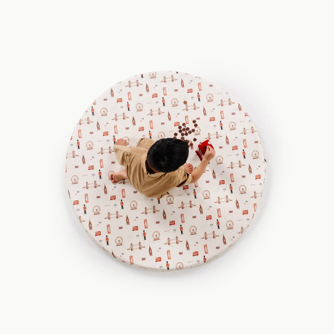 Overhead view of a child playing on the round London print padded play mat with Big Ben, guards, and red bus motifs