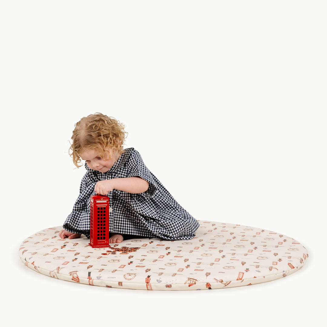 Toddler playing with a toy red phone booth on the round London print padded play mat
