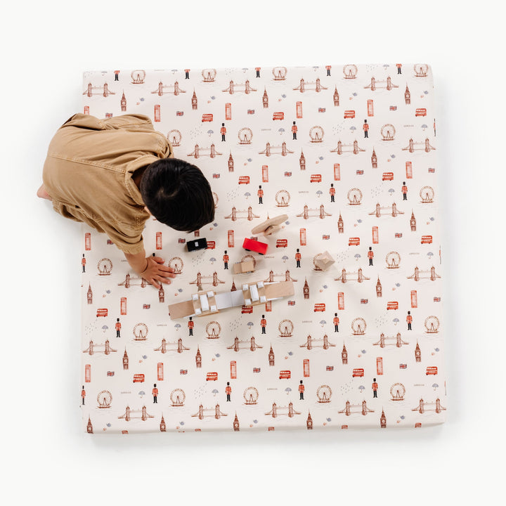 Overhead view of a child playing on the square London print padded play mat with a London skyline motif