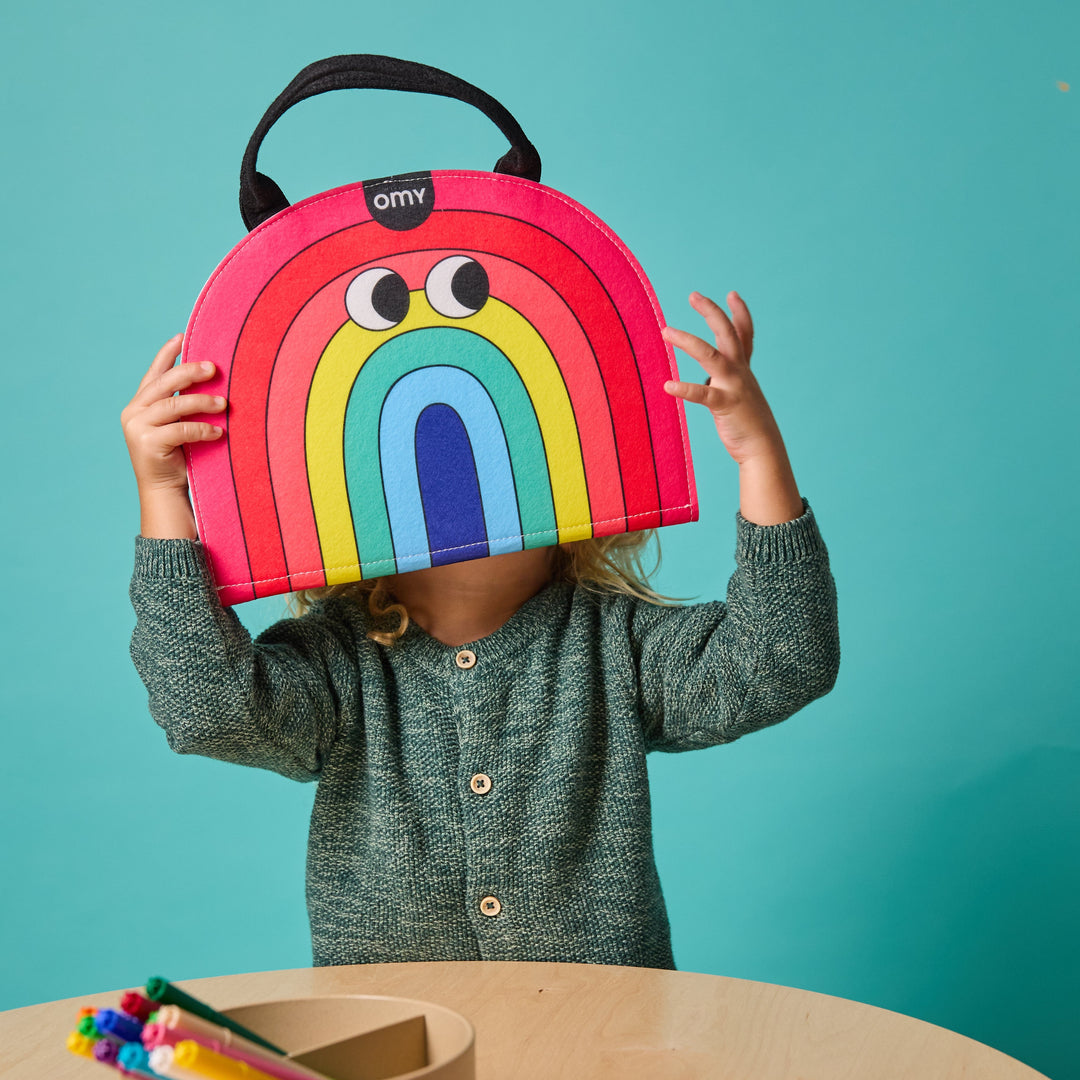 Child holding the rainbow-shaped felt Montessori kit up like a rainbow