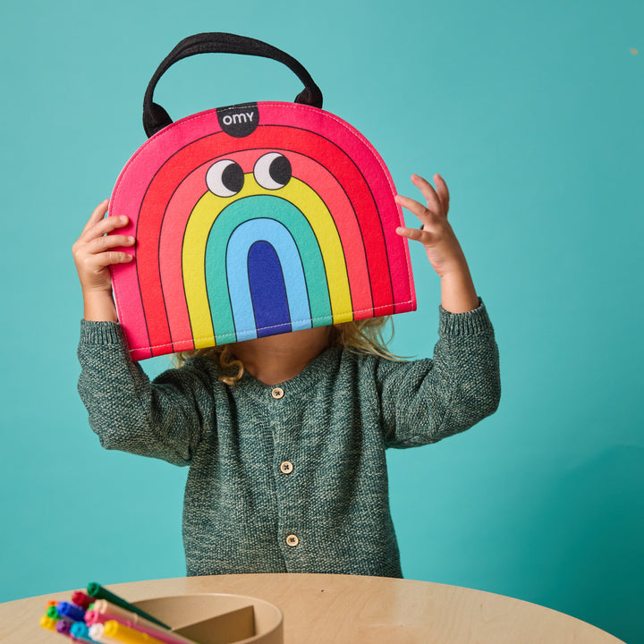 Child holding the rainbow-shaped felt Montessori kit up like a rainbow