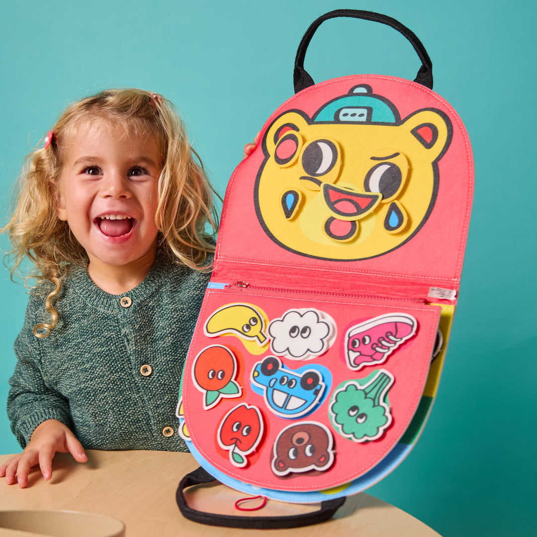 Smiling child with the opened felt Montessori kit showing a tiger face and shape activities