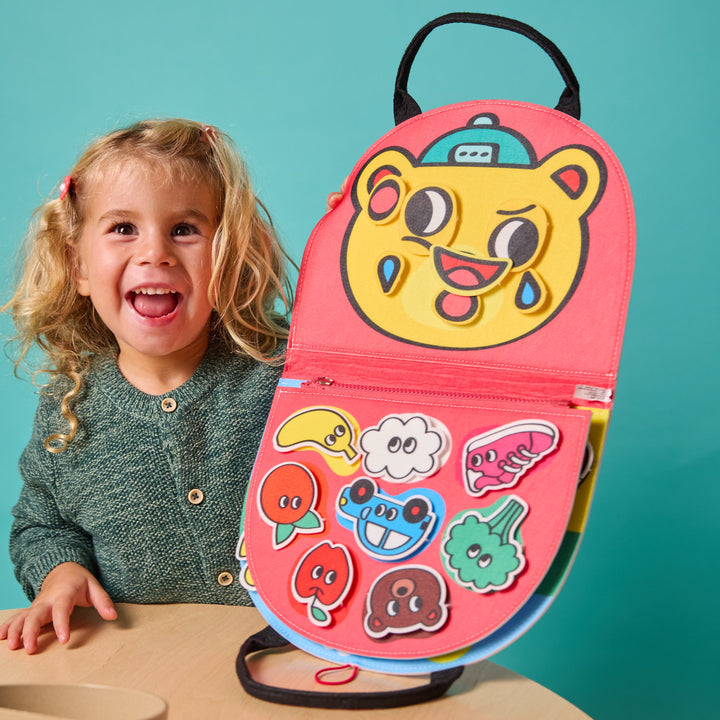 Smiling child with the opened felt Montessori kit showing a tiger face and shape activities