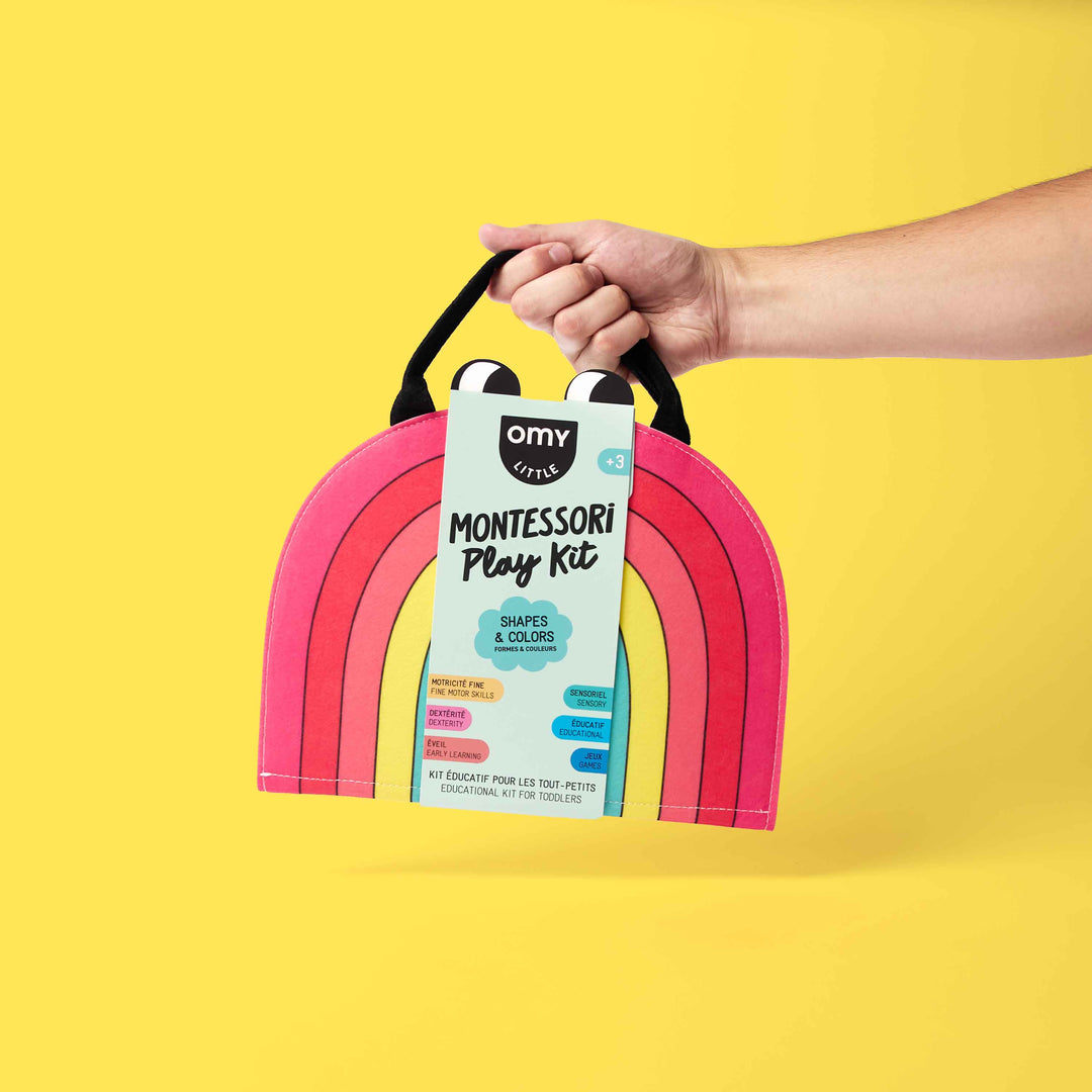 Hand holding the rainbow-shaped Shapes and Colors Montessori activity kit on a yellow background