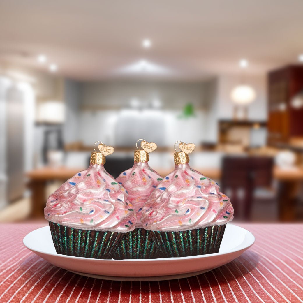 Three pink cupcake ornaments set on a white plate in a kitchen