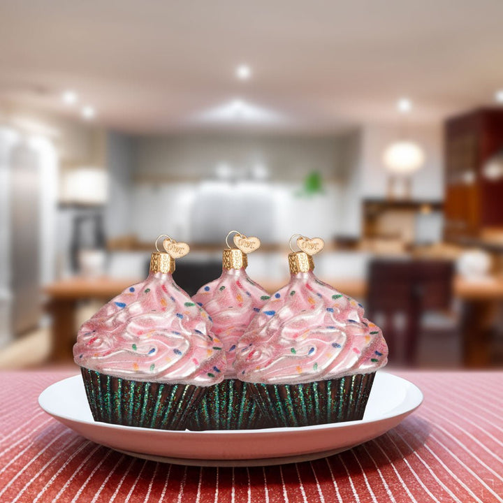 Three pink cupcake ornaments set on a white plate in a kitchen