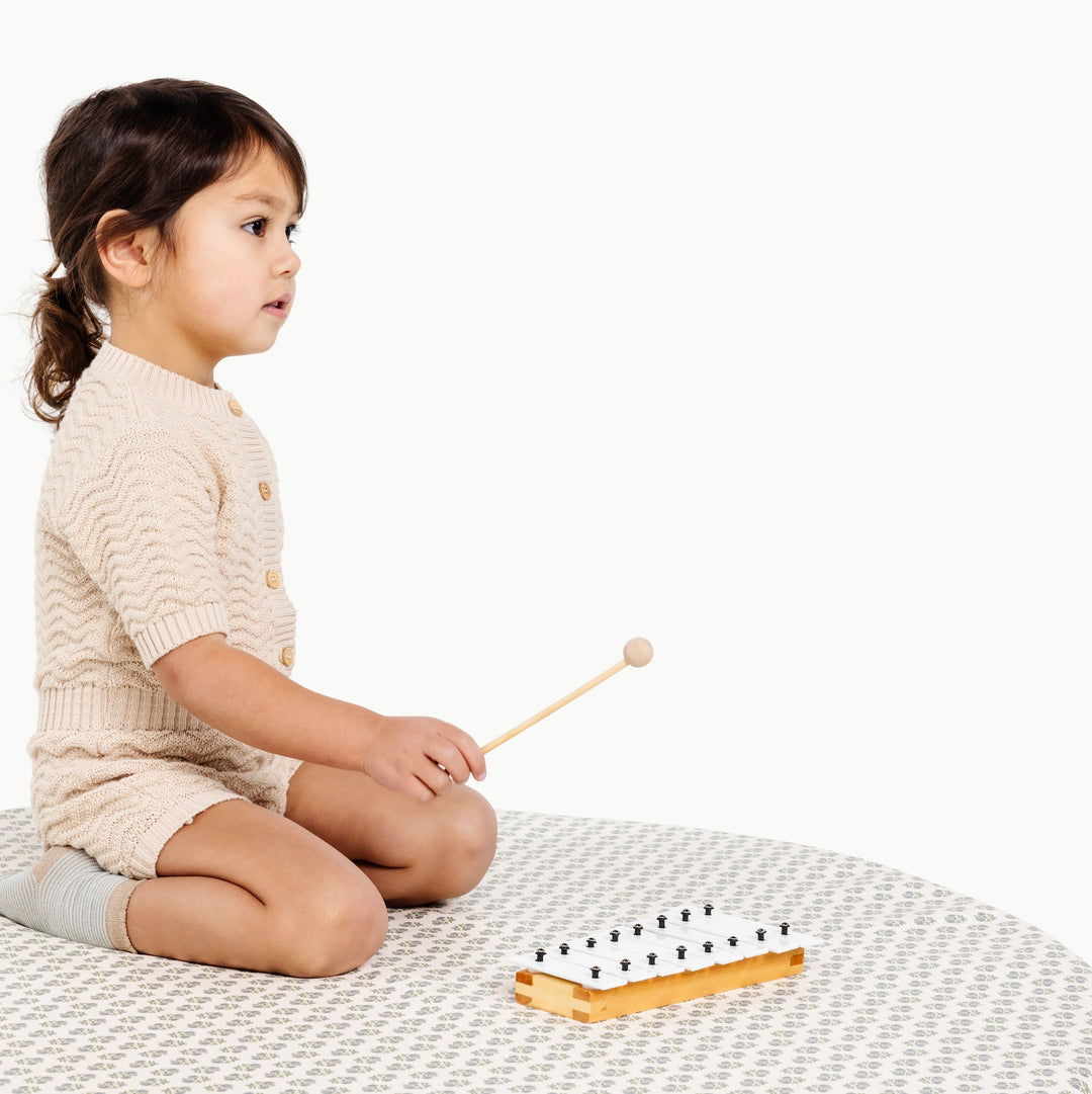 Blue floral block-print round padded play mat with a seated toddler and toy xylophone.