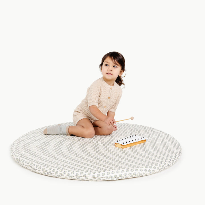 Blue floral block-print round padded play mat with a toddler and a toy xylophone.