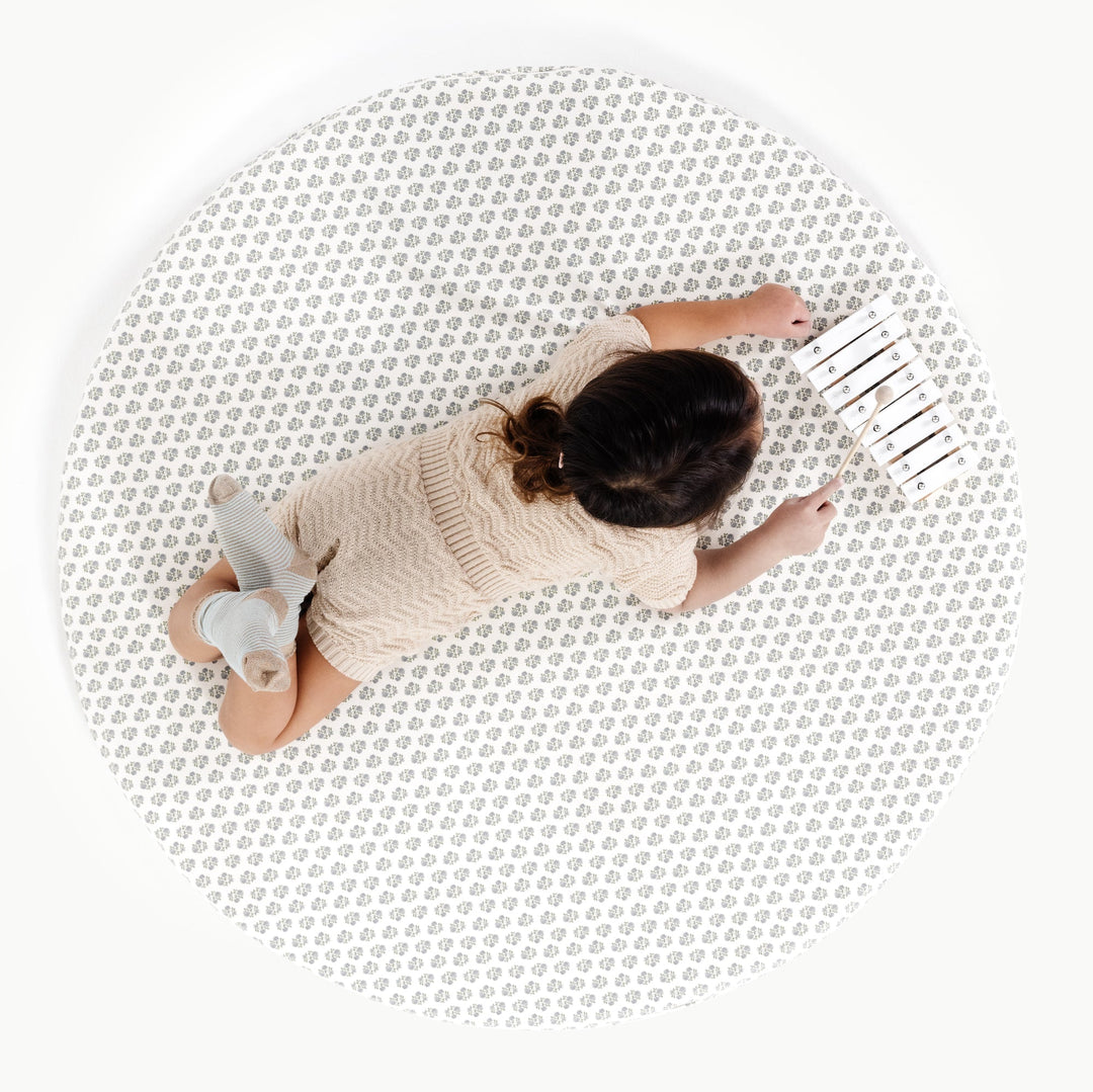 Blue floral block-print round padded play mat, overhead view with a toddler and toy.