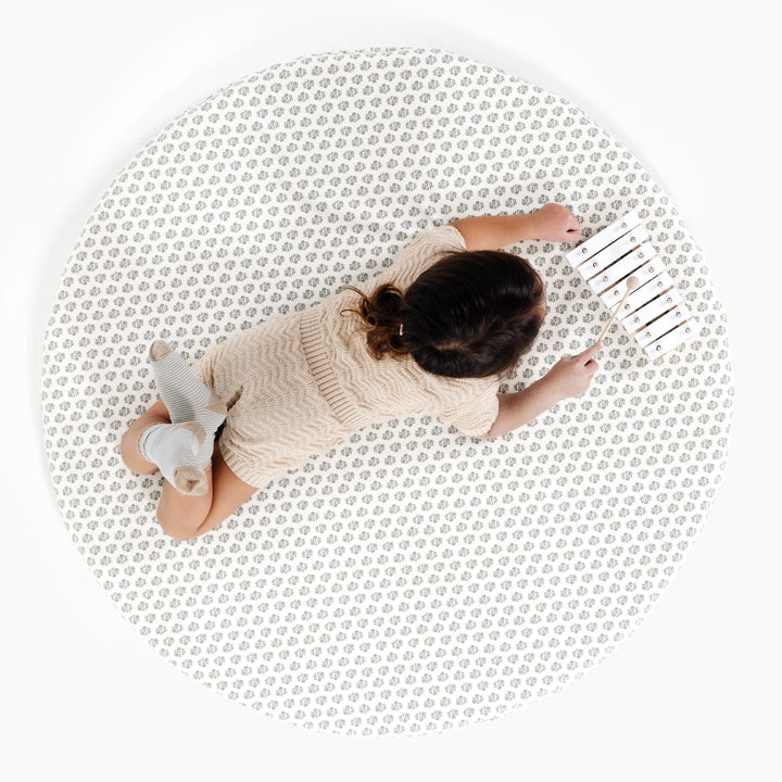 Blue floral block-print round padded play mat, overhead view with a toddler and toy.